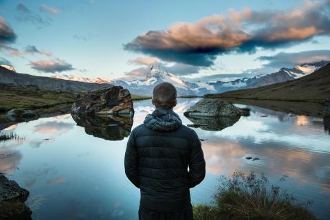 man looking across a lake to a mountain range